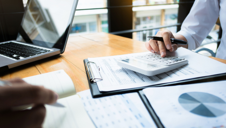 Two people sit at a desk reviewing papers with graphs and charts. 