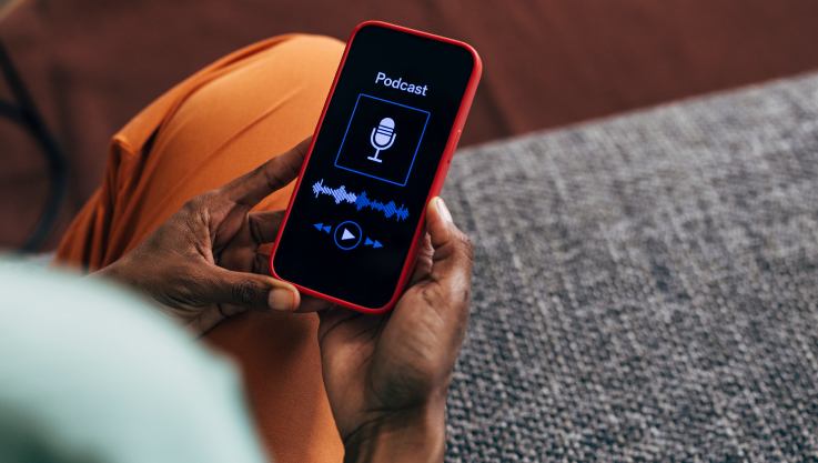 A person holds a phone in their hand. The screen shots a microphone with a sound wave and says "podcast" at the top. 